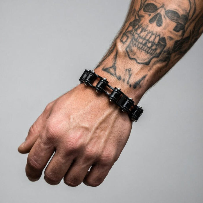 Black bracelet on a wrist with visible tattoos against a gray background